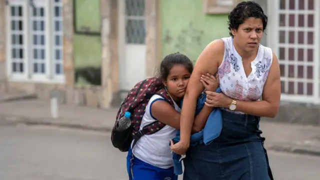 Una madre acompaña al colegio a su hija, que carga una mochila.