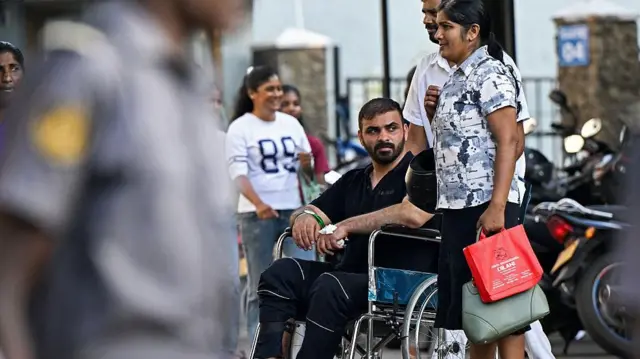 Tekerlekli sandalyede sakallı bir kişi itiliyor. Fotoğrafta başka kişiler de var.