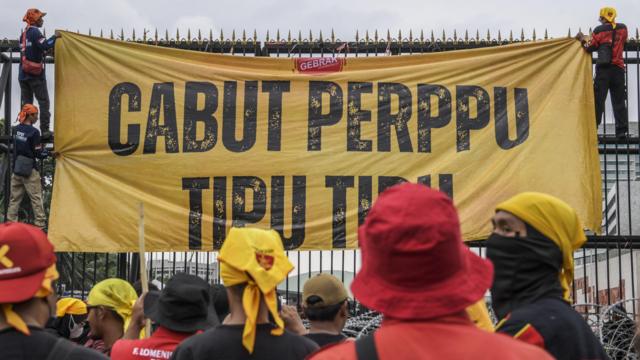 Pengunjuk rasa membentangkan spanduk saat berunjuk rasa di depan Gedung DPR, Senayan, Jakarta, Selasa (14/3/2023).