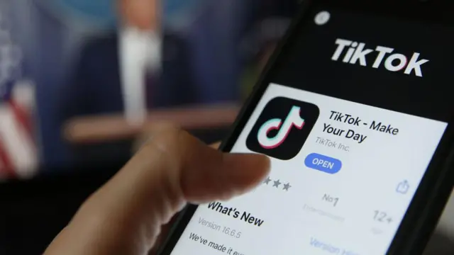 Celular com o aplicativo do TikToksportingbet boletoprimeiro plano, Donald Trump aparece desfocado ao fundo 