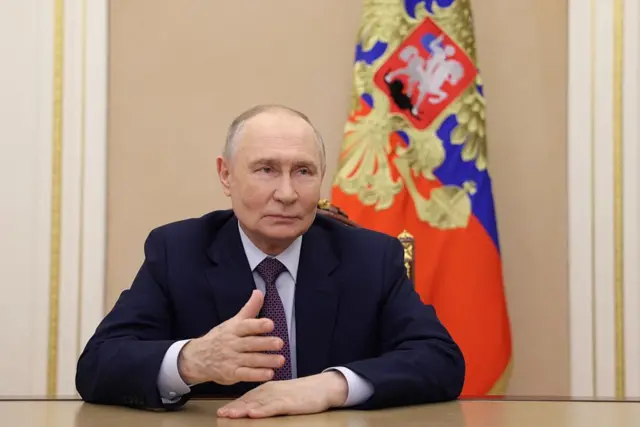 Vladimir Putin, sentado en un escritorio, con la bandera rusa detrás.