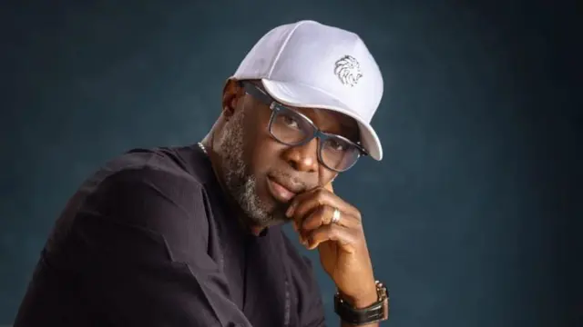 Adewale Ayuba, o de fila funfun, wọ ẹwu dudu. O figo soju, oruka ati aago sọwọ.