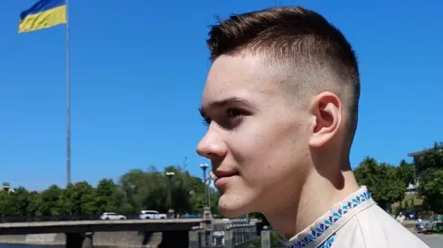 Крупним планом в анфас Дмитро Капуста. Хлопець дивиться з правої сторони ліворуч. Він вдягнений у вишиванку. 