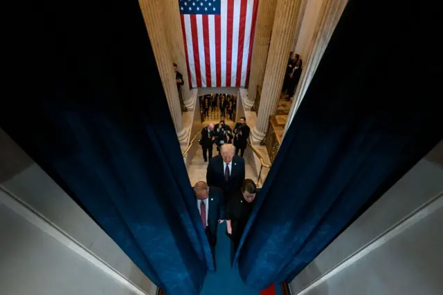 Foto tirada do alto mostra Trump e comitiva caminhandocomo ganhar dinheiro no esporte betdireção a porta, com bandeira dos EUA ao fundo