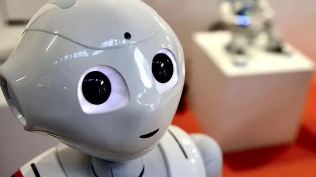 Un pequeño robot blanco de ojos grandes en el stand de la feria Maker Faire Roma.