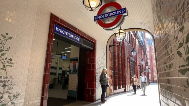 A 1930s style building with new white tiles and older brown tiles. A new Tube station entrance with the word Knightsbridge above and an Underground roundel in front.  