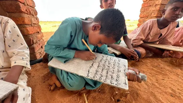 أربعة أطفال يتعلمون الكتابة في مدرسة نصبت في الساحة.