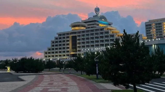 El hotel de fondo con un camino en el que se ven varios árboles y luces. No se ven personas