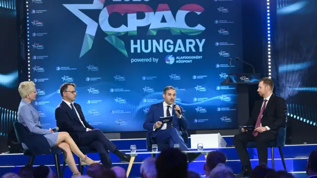 Panel czterech osób — jednej kobiety i trzech mężczyzn — siedzi na scenie przed publicznością. Za nimi widnieje baner z napisem „CPAC Hungary”.