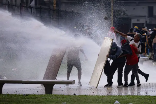 Manifestantes se defienden de un cañon de agua