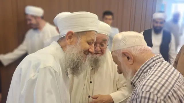 Beyaz sakallı üç adam yaklaşmış bir şeyler konuşuyor, ikisi de byeazlı ve sarıklı, üçüncüsü de takke giyinmiş, kareli gömlekli. 