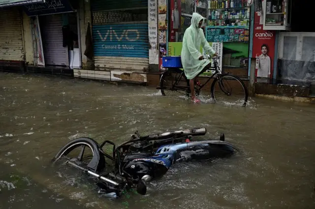 मुंबईतील मुसळधार पावसात पाण्यात बुडालेली एक बाईक आणि त्याच्या जवळून सायकल चालवत माणूस 