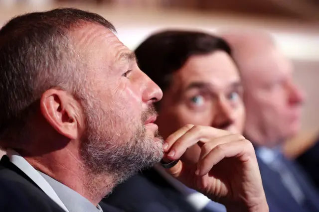 Мужчина с усами и бородкой внимательно слушает, держась за подбородок