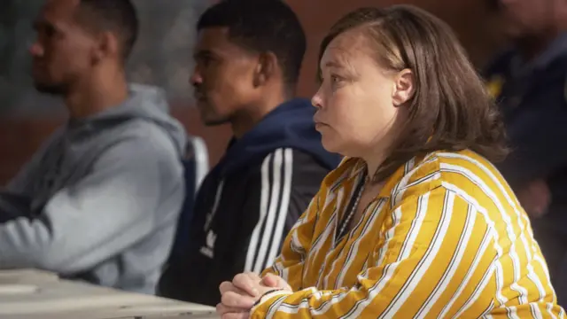 La mère de Joshlin Smith, vêtue d'une chemise rayée jaune, blanche et noire, est assise au tribunal, les mains jointes. A sa gauche se trouvent ses deux coaccusés.