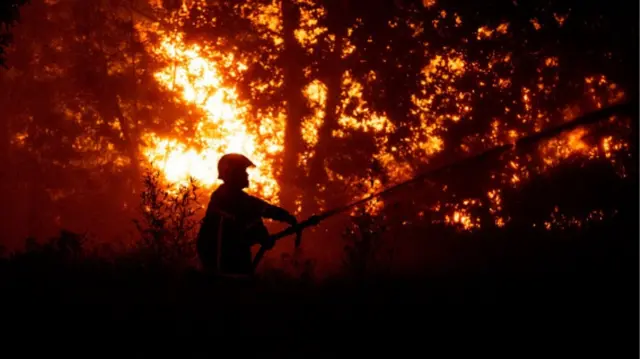 One firefighter dey spray water to quench di fire wey dey burn close to one residential area during one wildfire near Lege-Cap-Ferret, southwestern France,