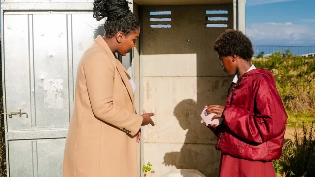 Tamara s'entretient avec une fille devant la porte d'une toilette