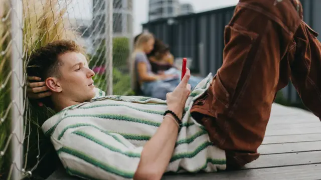 地面に横たわり、スマートフォンを手に持って画面をスクロールしている若い男性の写真