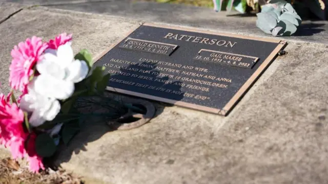 夫妻の名前と碑文を刻んだ墓石に、ピンクと白の花が供えられている