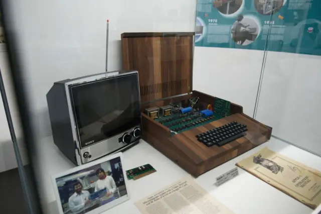O computador Apple 1 sobre uma mesa, ao lado de uma foto de Steve Jobs e Steve Wozniak