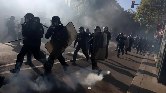 صورة تظهر أفراداً من شرطة مكافحة الشغب يركضون في الشارع ومحاطين بغاز مسيل للدموع.