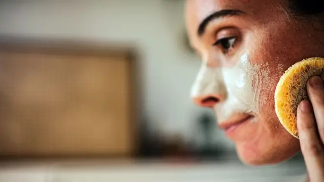 Mulher jovem passando creme no rosto com esponja