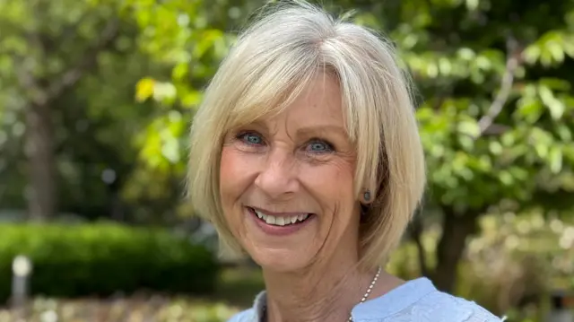 艾莉·墨菲(Aly Murphy)站在春日陽光下的樹蔭間,面帶微笑望向鏡頭。她擁有明亮的藍眼睛與金色頭髮,神情自信而愉悅。