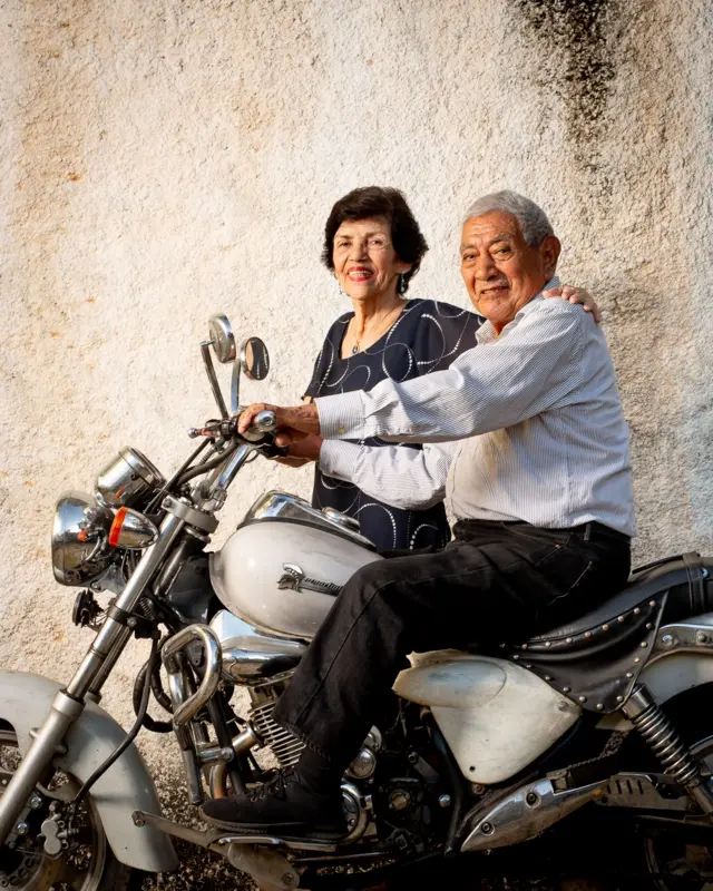 Retrato de Paula y Juan. Él está montado en una moto blanca y ella posa de pie a su lado. 