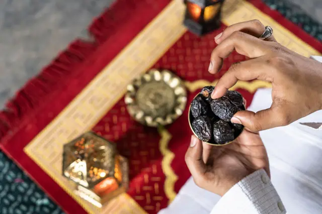 Un homme musulman sur un tapis de prière avec des dattes.