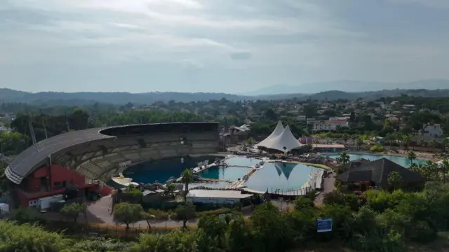 Foto aérea do parque Marineland, na França, mostra as piscinas e o anfiteatro à distância, rodeados com árvores e montanhas ao fundo