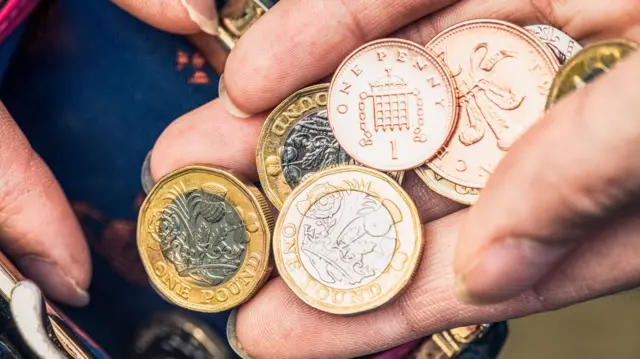 Selection of different coins in someone's hand, held above a purse