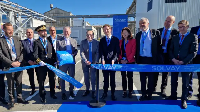 Solvay CEO Philippe Kerhen, wearing a suit and a blue tie, stands in the middle of a row dignitaries as he cuts the ribbon to open the expanded rare earths facility
