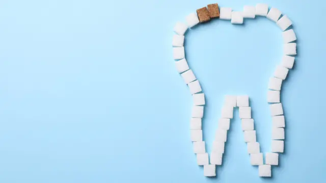 ilustración de varios cubos de azúcar que forman un diente. Dos de los cubitos son color marrón, mientras el resto son blancos. 
