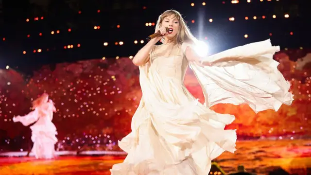 Taylor Swift dança em um vestido de baile na cor creme ornamentado durante sua turnê Eras de 2024