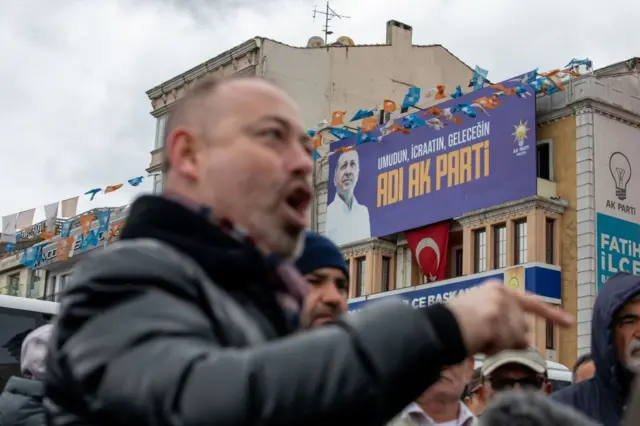 Bağıran bir adam, arkada Cumhurbaşkanı Erdoğan'ın posteri