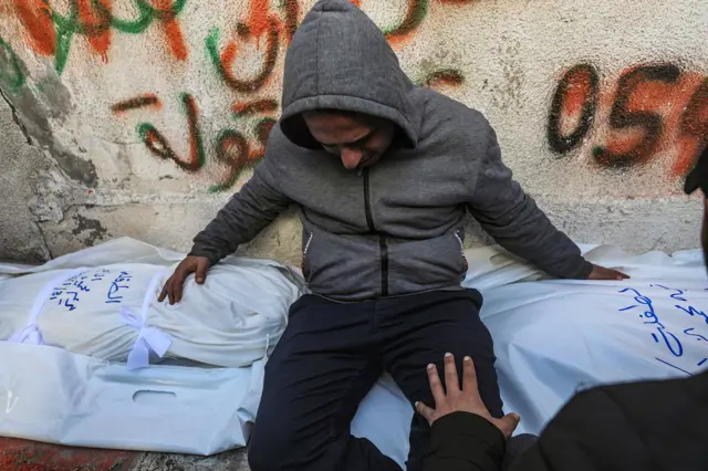 Un hombre llora y abraza dos mortajas.