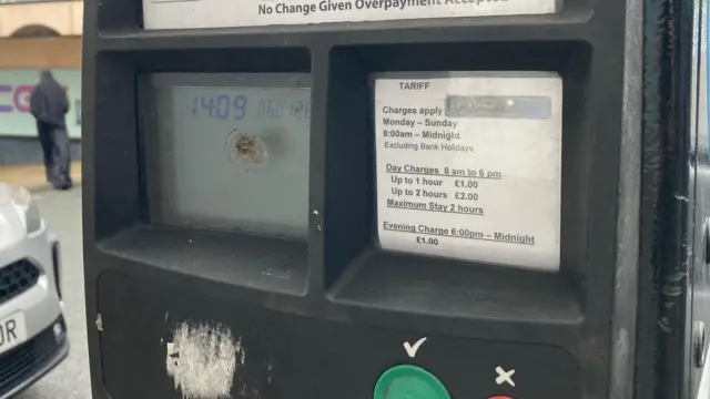 Un primer plano de una máquina expendedora de billetes de aparcamiento y las tarifas de cobro.