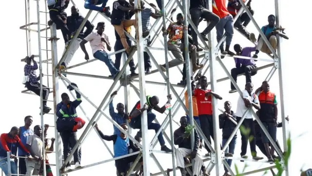 Abantu baje kwibuka bahagaze ku munara kugira ngo bashobore kureba ibirimo kubera ku kibuga cya 'Jomo Kenyatta Stadium' i Kisumu. Ifoto yo ku itariki ya 18 Ukwakira (10) mu mwaka wa 2025. 