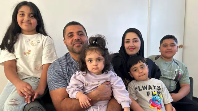 The Rahimi family sitting on a sofa. From left to right they are ten-year-old Omra, Habib who is holding one-year-old Samreen, Nelab, four-year-old Hamdullah and eleven-year-old Hizbullah.