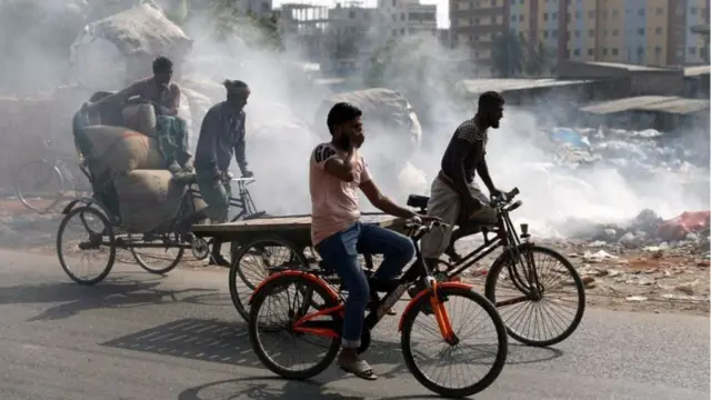 রাস্তার পাশে বর্জ্য পোড়ানো হচ্ছে, ভ্যানচালকরা নাকে হাত দিয়ে আছে।