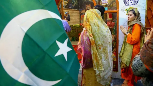 একটি মন্দিরে দুই নারী দাঁড়িয়ে আছেন, পাশে পাকিস্তানের পতাকা
