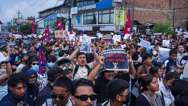 A large group of young people fill a street, holding posters and Nepalese flags, on 8 September 2025. One poster reads: 'Wake up Nepal - Stop loot, start work'.