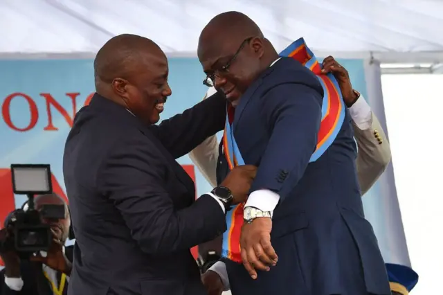 L’ancien président Joseph Kabila (G), drape le président nouvellement investi, Félix, le 24 janvier 2019, de l'écharpe présidentielle lors de la remise officielle des instruments du pouvoir à la présidence à Kinshasa.