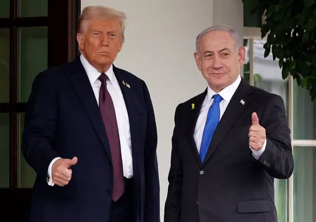Donald Trump y BEnjamin Netanyahu miran al frente y levantan sus pulgares. Ambos visten trajes oscuros y corbata.