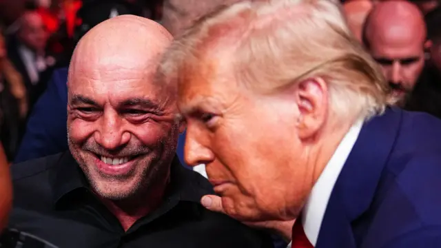 Joe Rogan’ın gülümsüyor. Donald Trump, elini Rogan’ın omzuna koymuş.