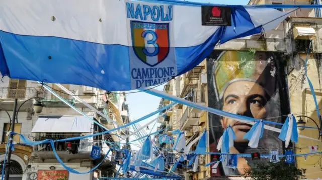 Spanduk merayakan kemenangan Scudetto Napoli yang sudah dekat digantung di depan mural San Gennaro di Napes