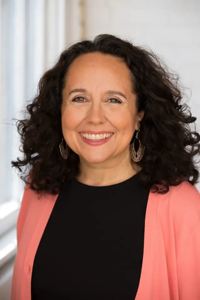 سيدة ذات شعر بني داكن تنظر مبتسمةً إلى الكاميرا