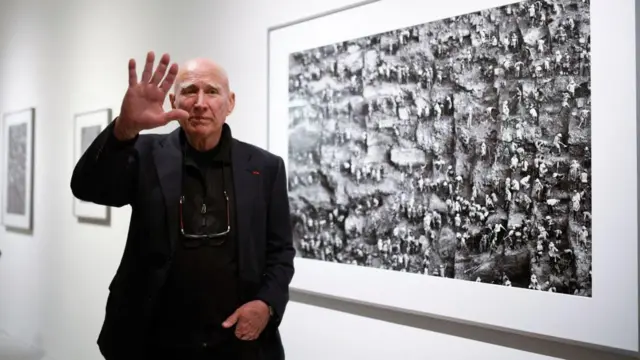 Sebastião Salgado em frente a uma foto de Serra Pelada. 