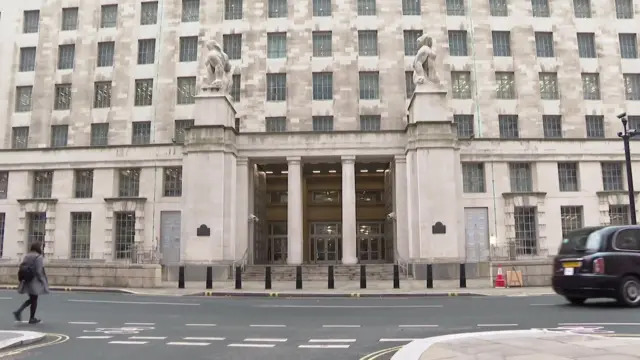 The Ministry of Defence main building on Whitehall in London, with its stone statues flanking the columned entrance and a black cab passing