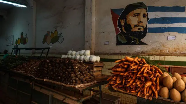 Mercado agropecuario en Cuba con una pintura de Fidel Castro sobre una bandera cubana en la pared. 