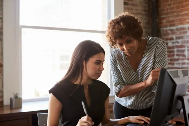 Duas mulheres trabalhandocaçaniquelfrente a uma telacaçaniquelcomputador